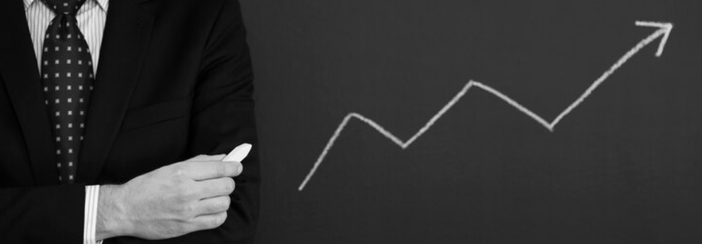 Business professional standing confidently with arms crossed, next to a chalkboard showing an upward growth arrow, symbolising success and progress.